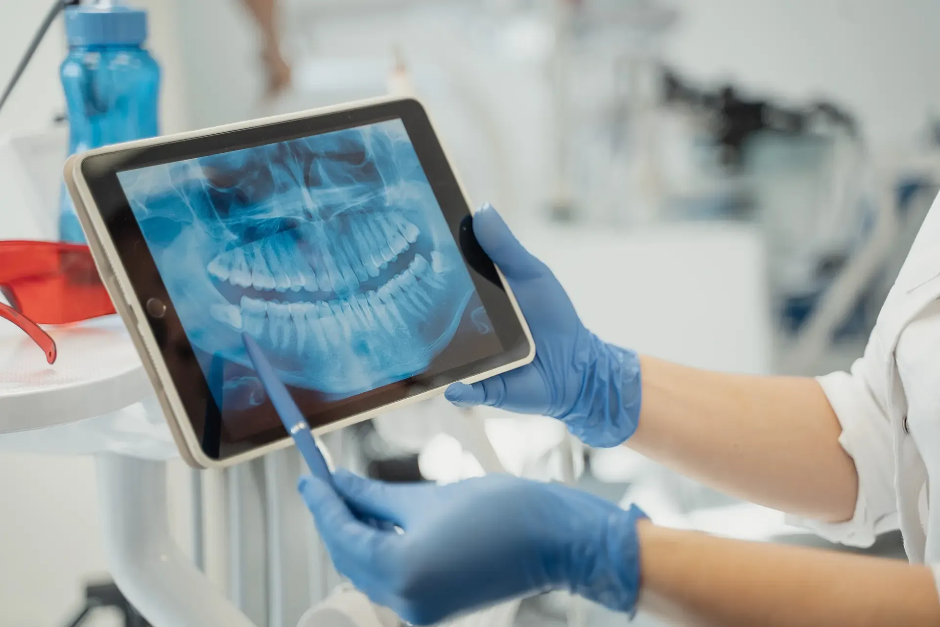 Dentist in gloves pointing at a dental X-ray on a tablet with a stylus
