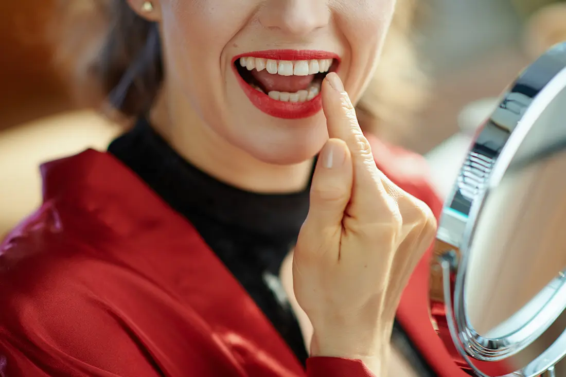 Woman smiling while checking her teeth in a handheld mirror