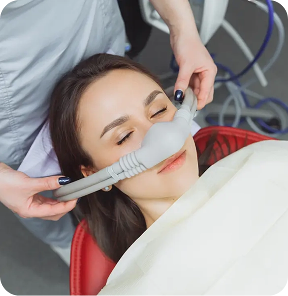 Patient relaxed in a dental chair with a nitrous oxide sedation mask while a team member adjusts equipment