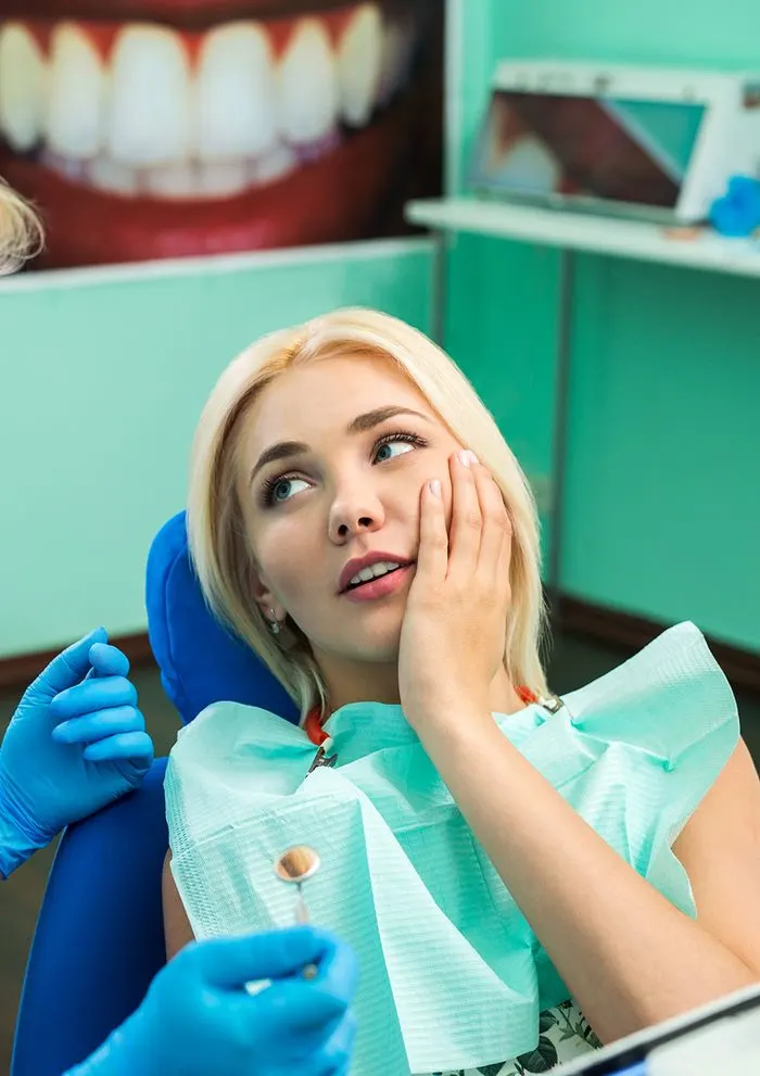 Woman in a dental chair holding her cheek while a dentist examines her during same-day emergency care